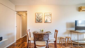 Ein Essbereich mit einem runden Tisch, Korbstühlen und zwei gerahmten Kunstwerken an der Wand.