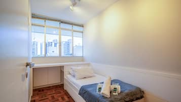 Un dormitorio pequeño con ventana, cama y una zona de escritorio.