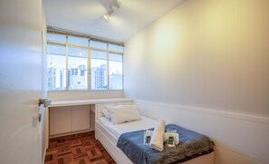 A compact bedroom with a window, a bed, and a small desk area.