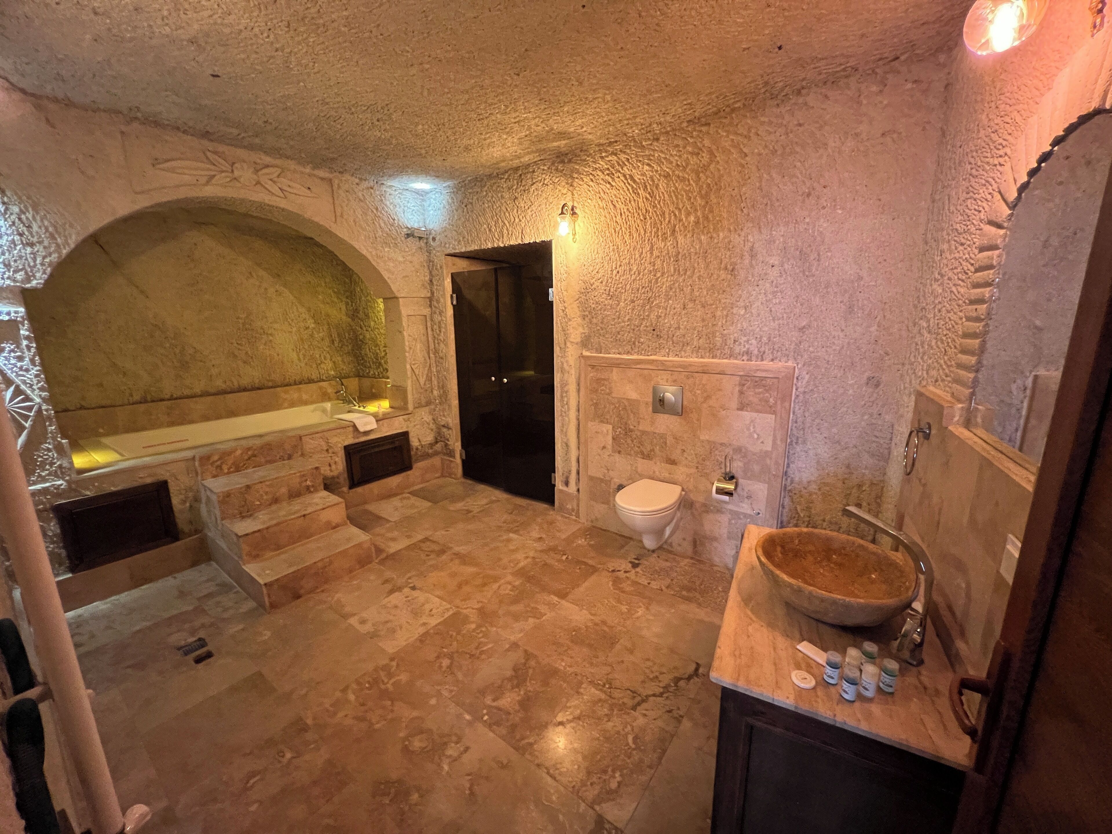 A stone-walled bathroom with a bathtub, toilet, and sink.