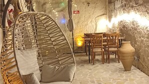 Een terras met stenen tegels, een rieten stoel en houten tafels.