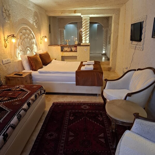 A bedroom with a bed, a nightstand, a chair, a table, and a bathroom visible through an archway. - TATLI KAYA OTEL (Urgup)