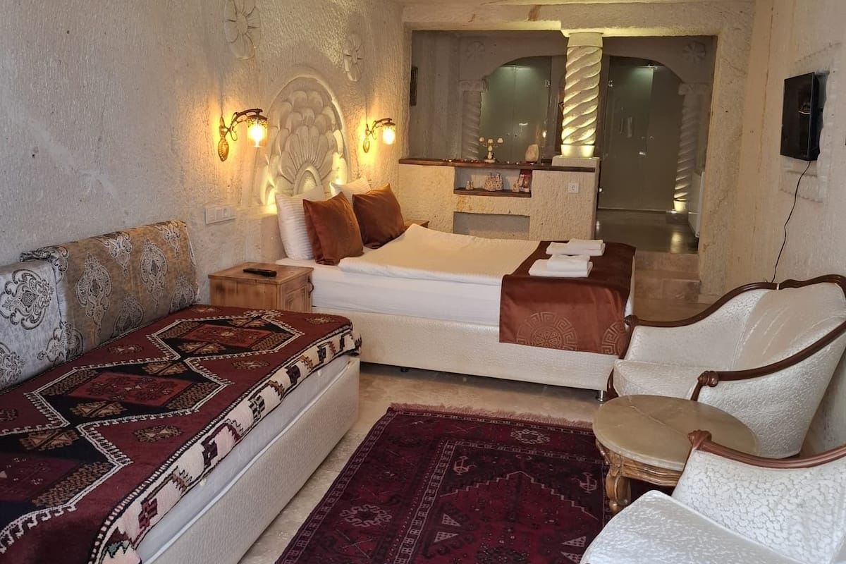 A hotel room with a bed, sofa, armchair, and a decorative rug.