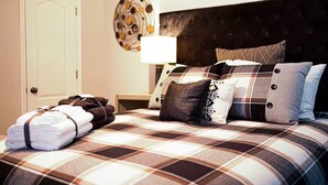 Un lit bien fait, recouvert d’une couverture à carreaux, une pile de serviettes pliées et un élément décoratif accroché au mur.