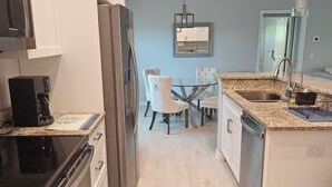 A modern kitchen with white cabinets, stainless steel appliances, a glass dining table with chairs, and a pendant light.