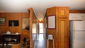 Ein Korridor mit Holzvertäfelung, einem Schreibtisch mit Büchern, einem Stuhl, einem weißen Kühlschrank und einem gerahmten Bild an der Wand.
