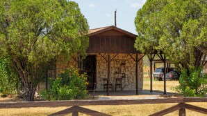 Ein rustikales Steinhaus mit Holzdach, umgeben von Bäumen und einem Holzzaun.