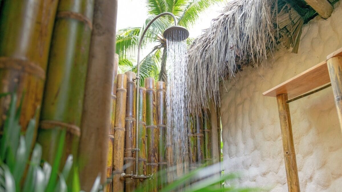 Une douche avec un espace clos en bambou et un toit de chaume.
