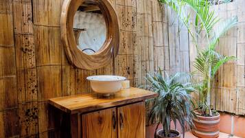 A rustic bathroom with wooden walls, a wooden vanity, a round mirror, and a potted plant.