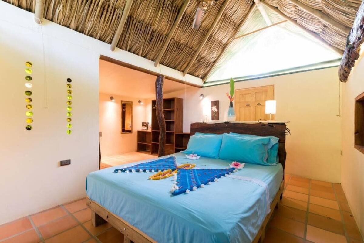 A bedroom with a bed, a wooden headboard, a thatched roof, and a wall with circular light fixtures.