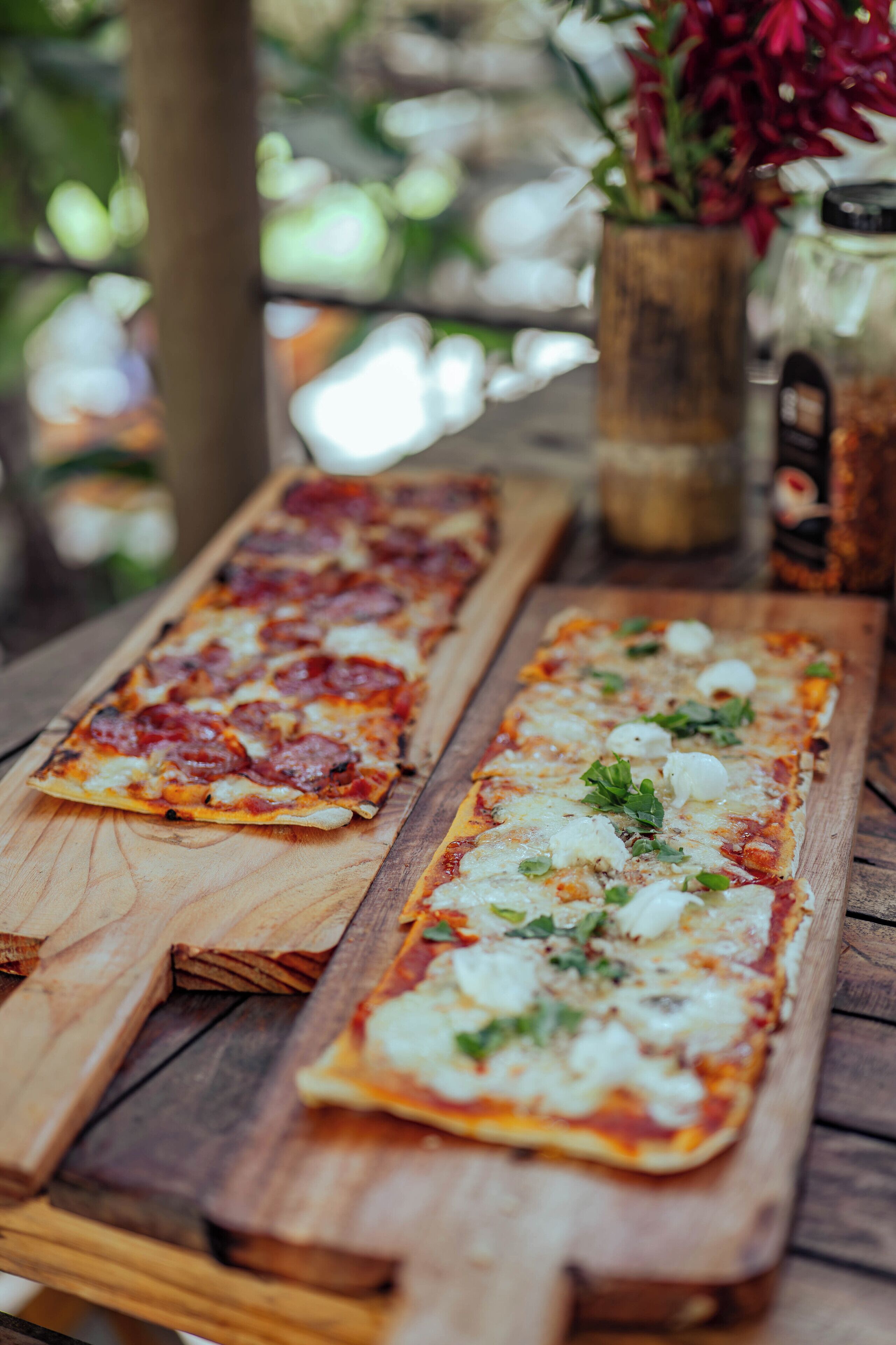 Two rectangular pizzas on a wooden board, one with pepperoni and the other with cheese and herbs.