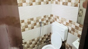 Et badeværelse med toilet, håndvask og bruser. Væggene er fliset med et skakmønster.