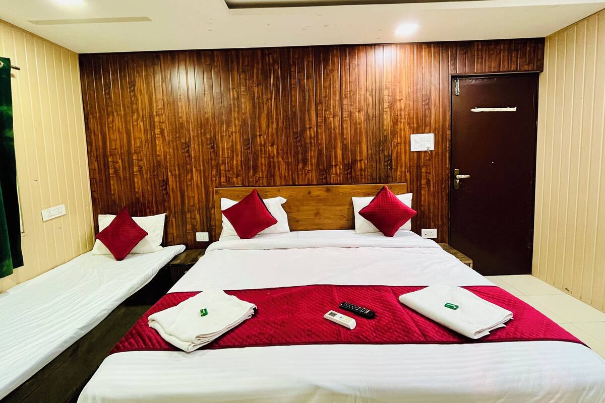 A hotel room with a wooden panel wall, a large bed with red and white bedding, two smaller beds, and a door.