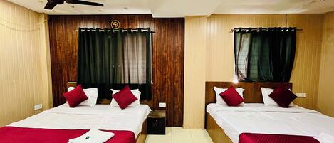 A hotel room with two beds, each with a red bedspread and white linens. There is a ceiling fan above the beds, and the room has wooden paneling on the walls.