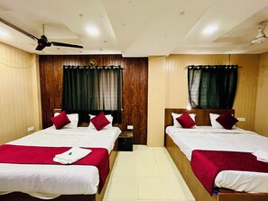 A hotel room with two beds, each with a red bedspread and white linens. There is a ceiling fan above the beds, and the room has wooden paneling on the walls.