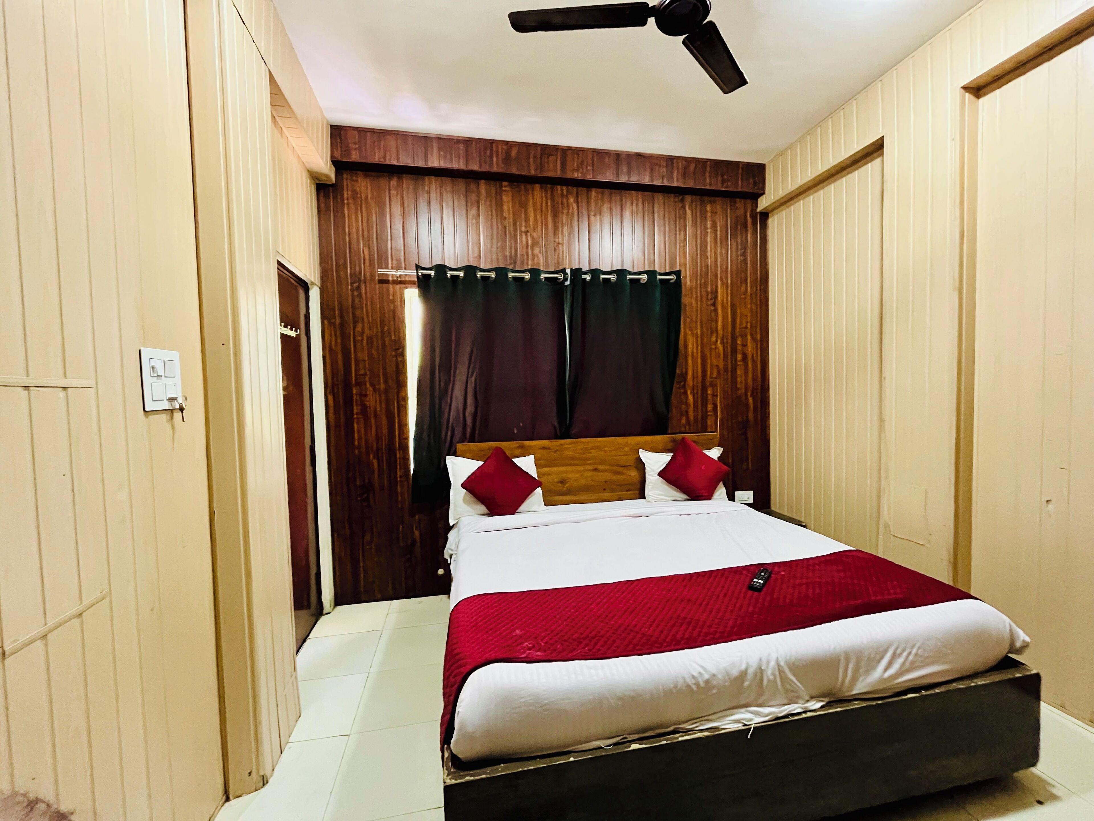 A bedroom with a wooden headboard, a bed with white and red bedding, a ceiling fan, and a light switch on the wall.