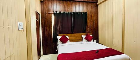 A bedroom with a wooden headboard, a bed with white and red bedding, a ceiling fan, and a light switch on the wall.