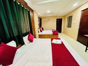 A hotel room with two beds, each with white linens and red accents, a wooden headboard, and a large window with blinds.