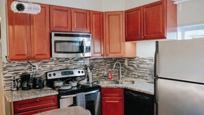 A compact kitchen with wooden cabinets, a stainless steel microwave, a stove, and a refrigerator. - Dream / King Bed / 120" Projector / Canopy Bed (Philadelphia)