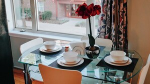 A dining area with a glass table, white chairs, and a vase with red flowers. - Dream / King Bed / 120" Projector / Canopy Bed (Philadelphia)