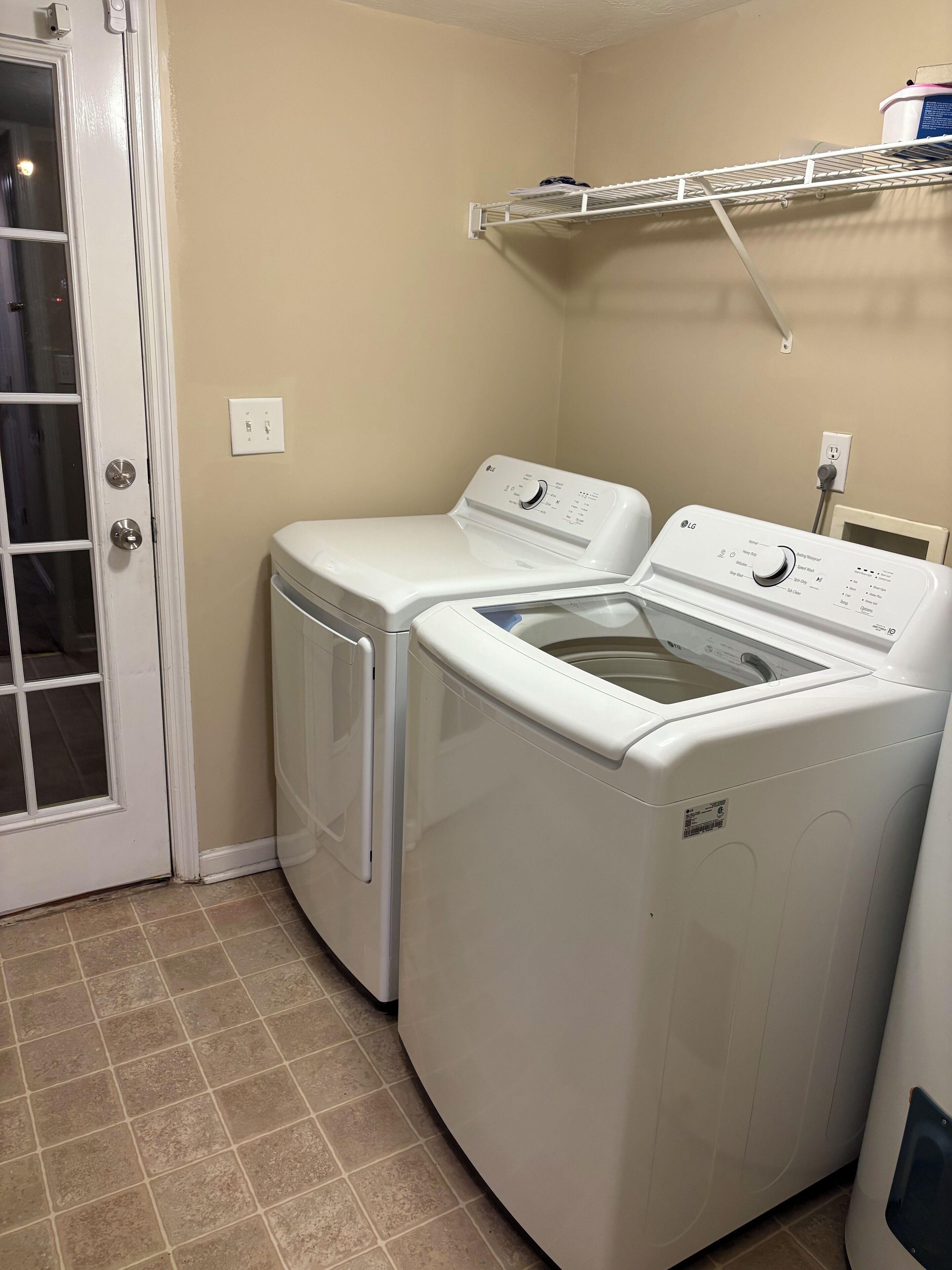 A laundry room with two front-loading washing machines, a drying rack, and a door with a glass panel.
