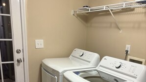 Una sala de bugaderia amb dues rentadores de càrrega frontal, un escorredor i una porta amb un panell de vidre.