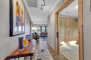 A hallway with a wooden table, a glass of orange juice, and a colorful abstract painting.