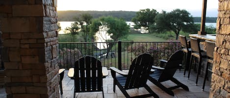 A balcony with two Adirondack chairs, a stone wall, and a view of a lake and trees.