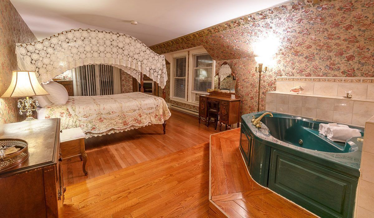 Een slaapkamer met een groot bed, een kaptafel met spiegel, een groen bad en een houten dressoir.