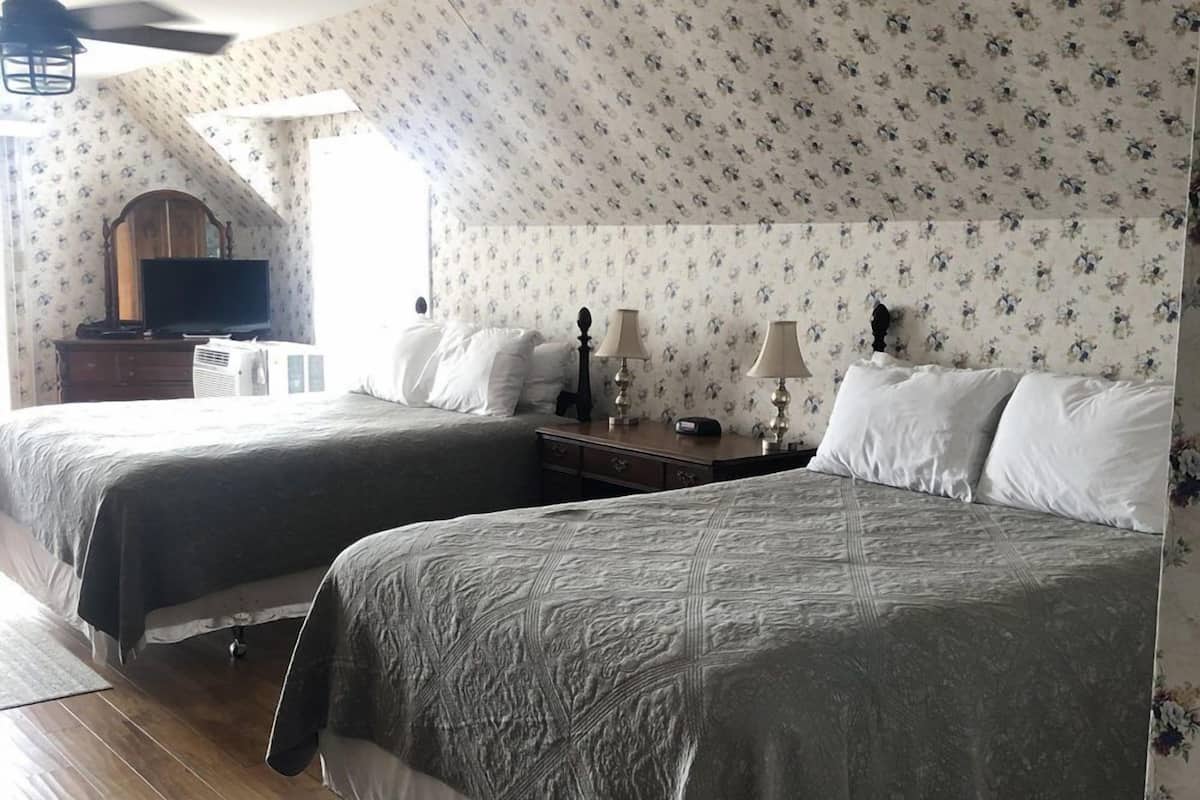 Habitación de hotel con dos camas, un aparador, un televisor y un ventilador de techo.