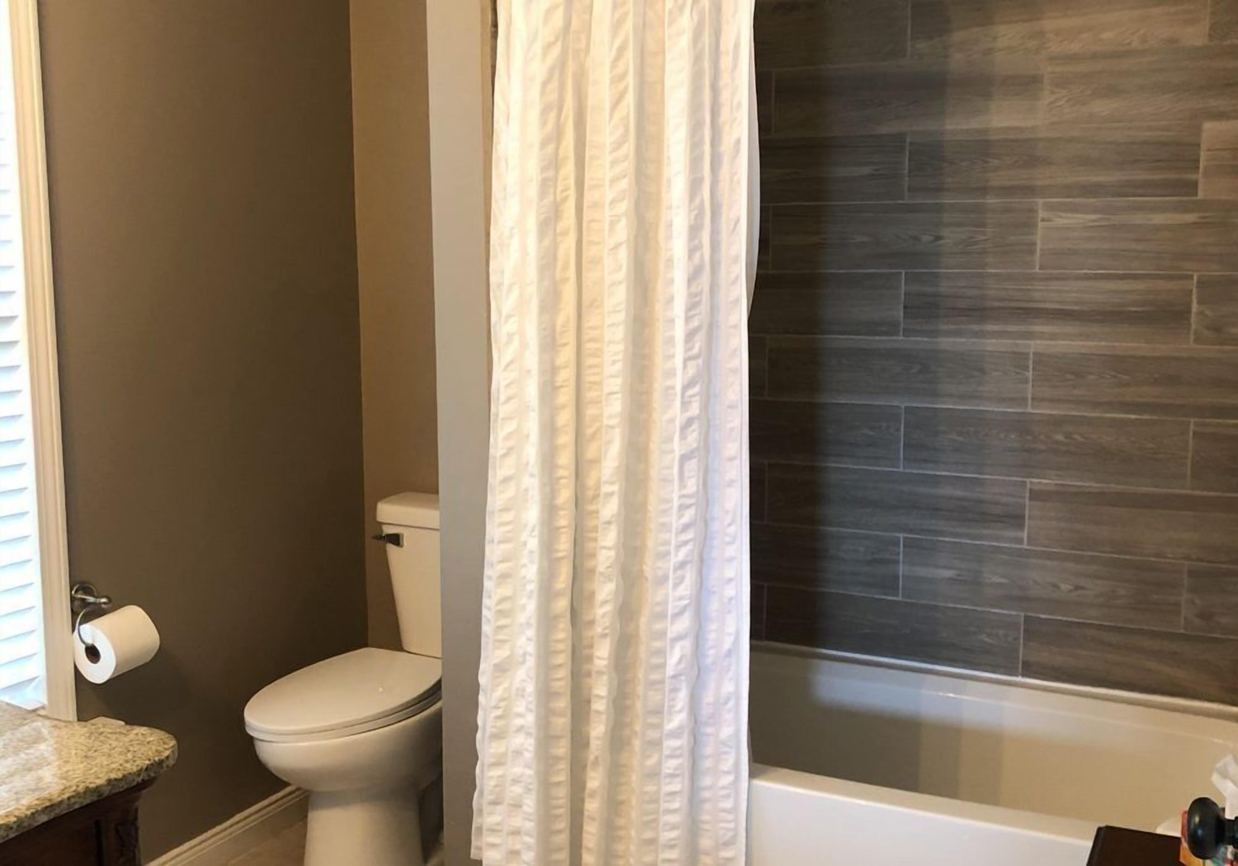 A bathroom with a toilet, a shower curtain, and a bathtub with a dark wood-patterned wall.