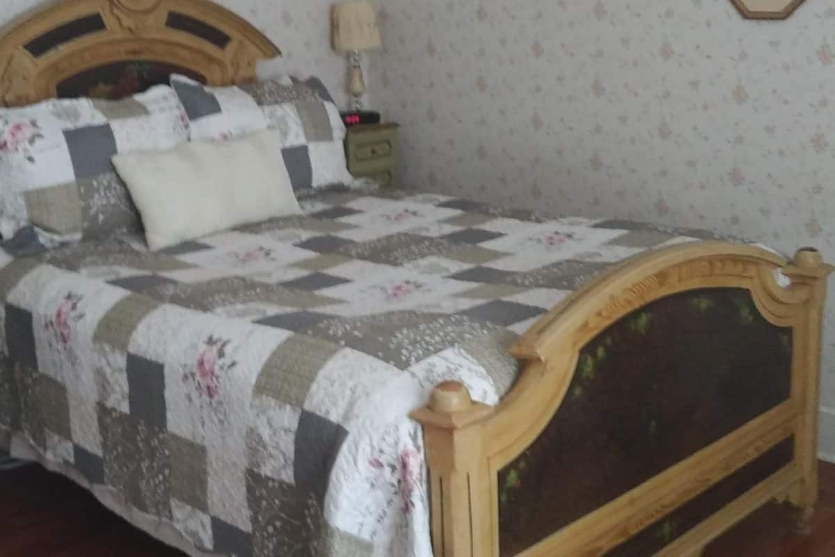 Una cama con colcha, cabecera de madera y una mesita de noche con lámpara.