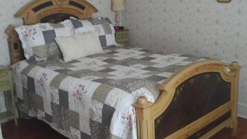 A bed with a quilt, wooden headboard, and a nightstand with a lamp.