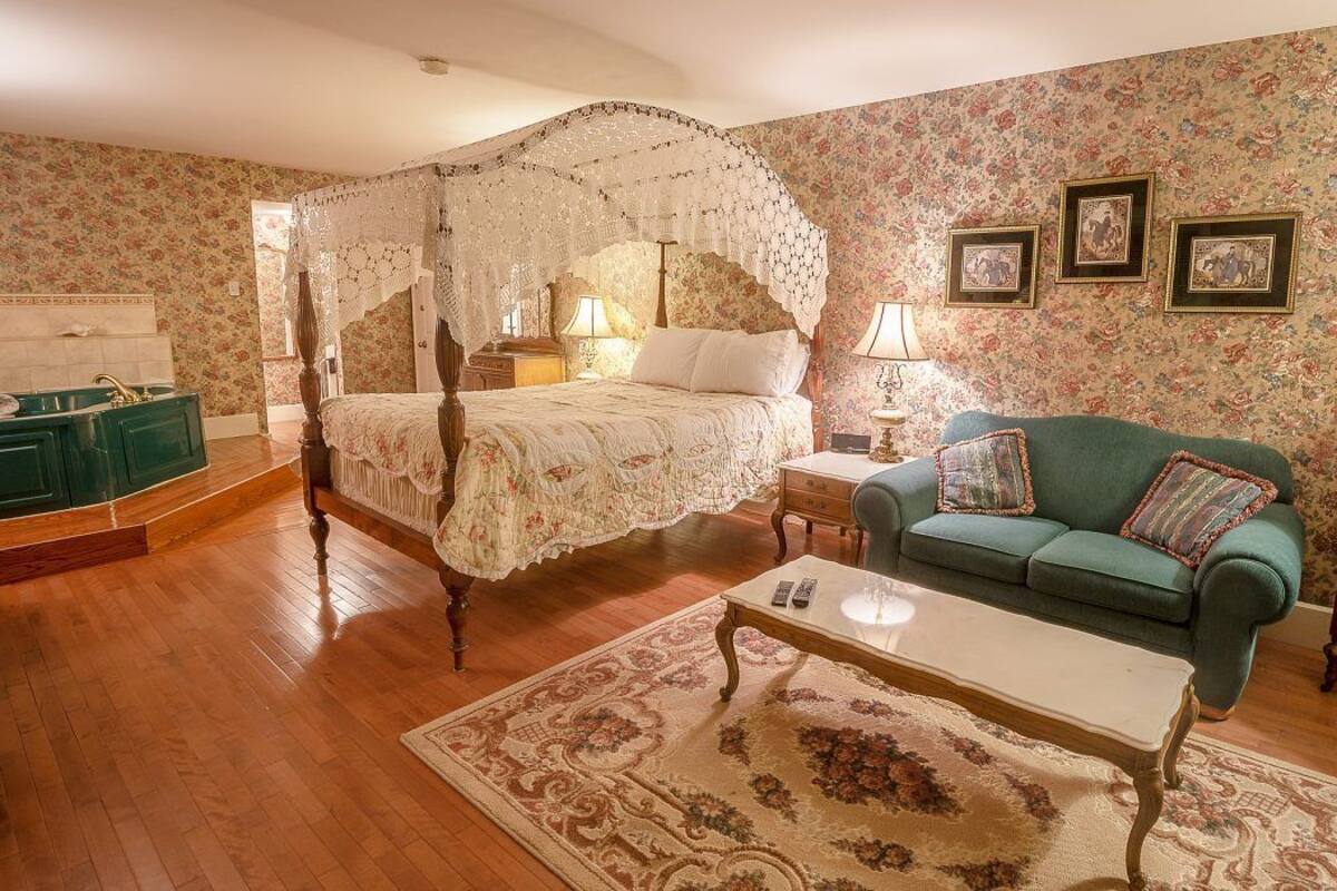 Un dormitorio con cama con dosel, un sofá verde, un aparador de madera y papel tapiz floral.