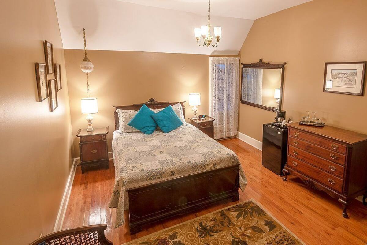 Un dormitorio con cama, cómoda, mesitas de noche y una araña.