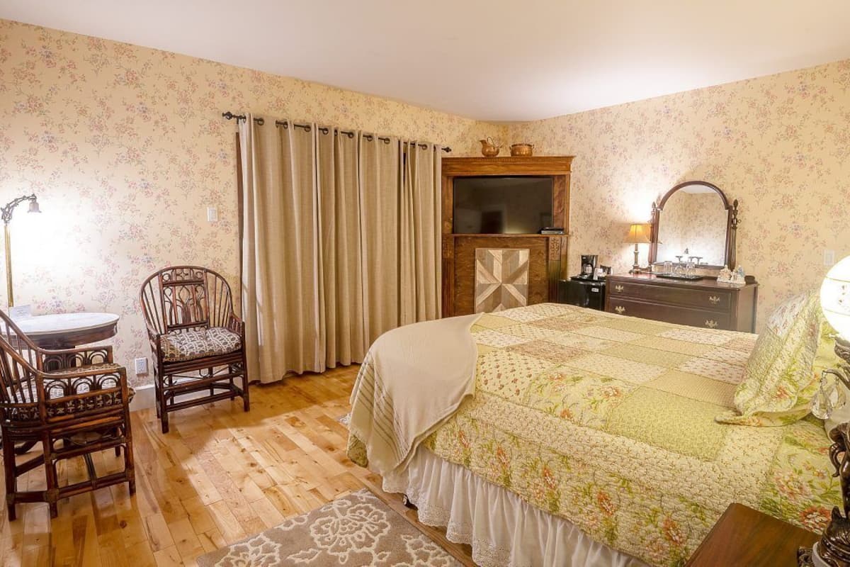 Un dormitorio con cama, cómoda de madera, silla, escritorio, espejo y lámpara.