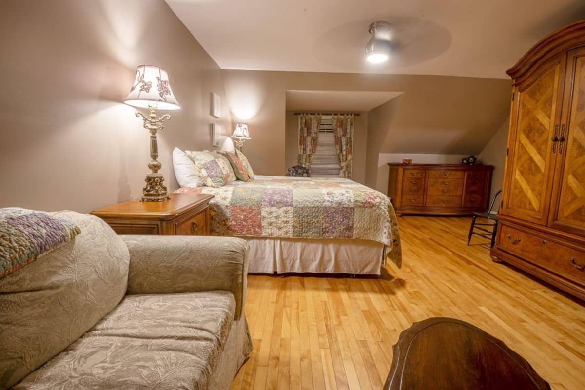Un dormitorio con una cama, dos mesitas de noche con lámparas, un armario de madera y una escalera que sube a un nivel superior.