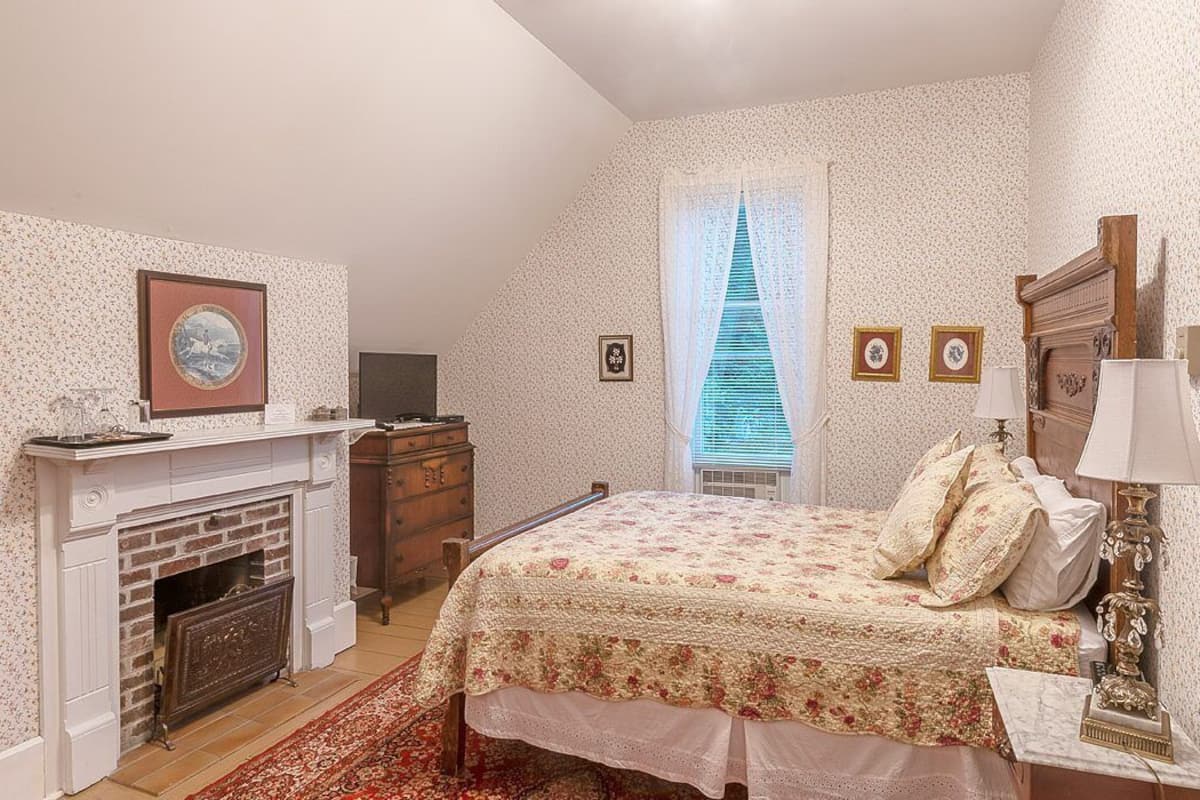 Un dormitorio con cama, chimenea, cómoda y ventana con cortinas.