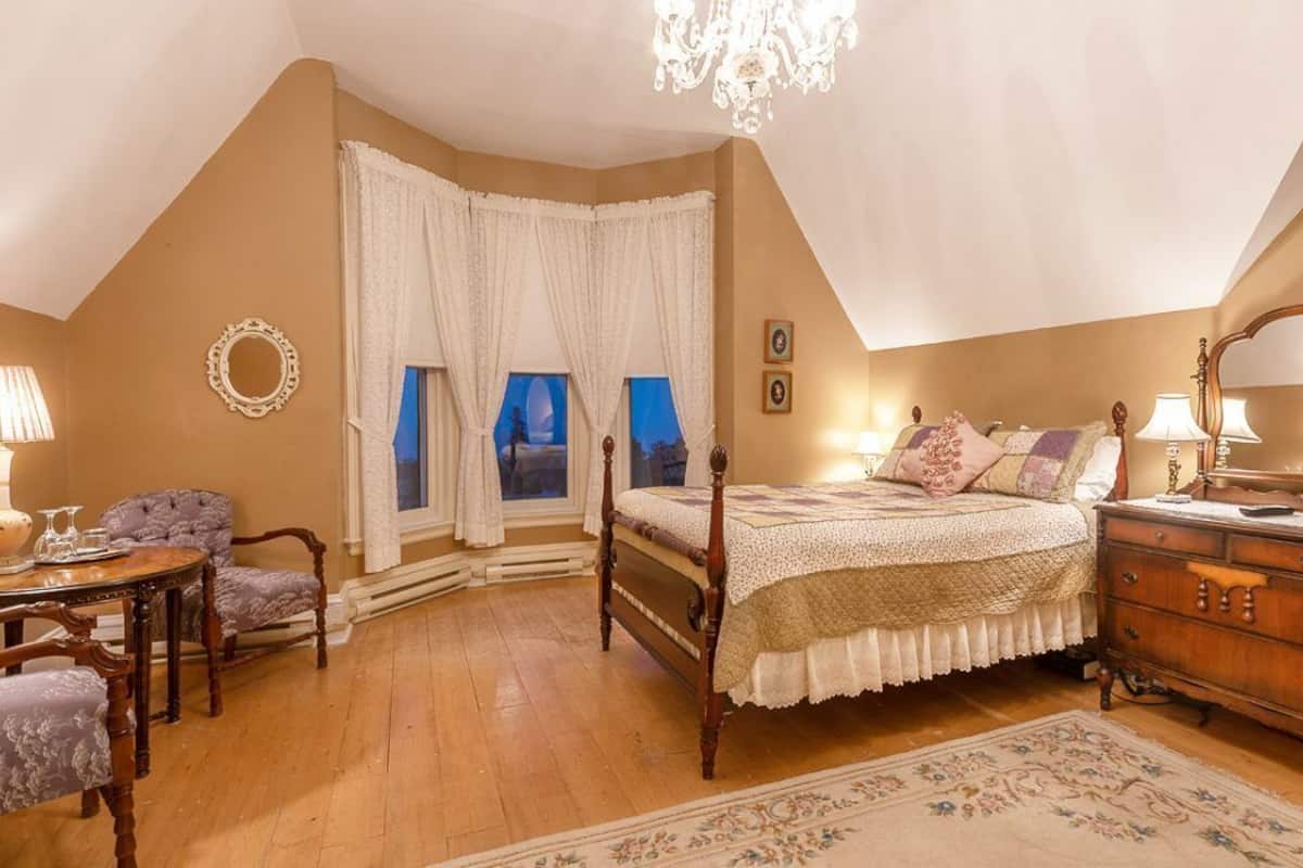 Un dormitorio con una cama de madera, un aparador, una silla, una mesa y una araña.