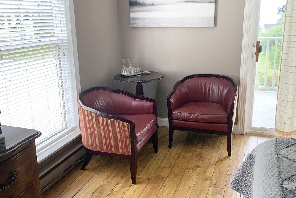 Een kamer met twee leren stoelen, een klein rond tafeltje met glazen, en een schilderij aan de muur.