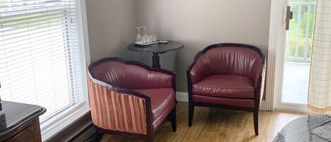 A room with two leather chairs, a small round table with glasses, and a painting on the wall.