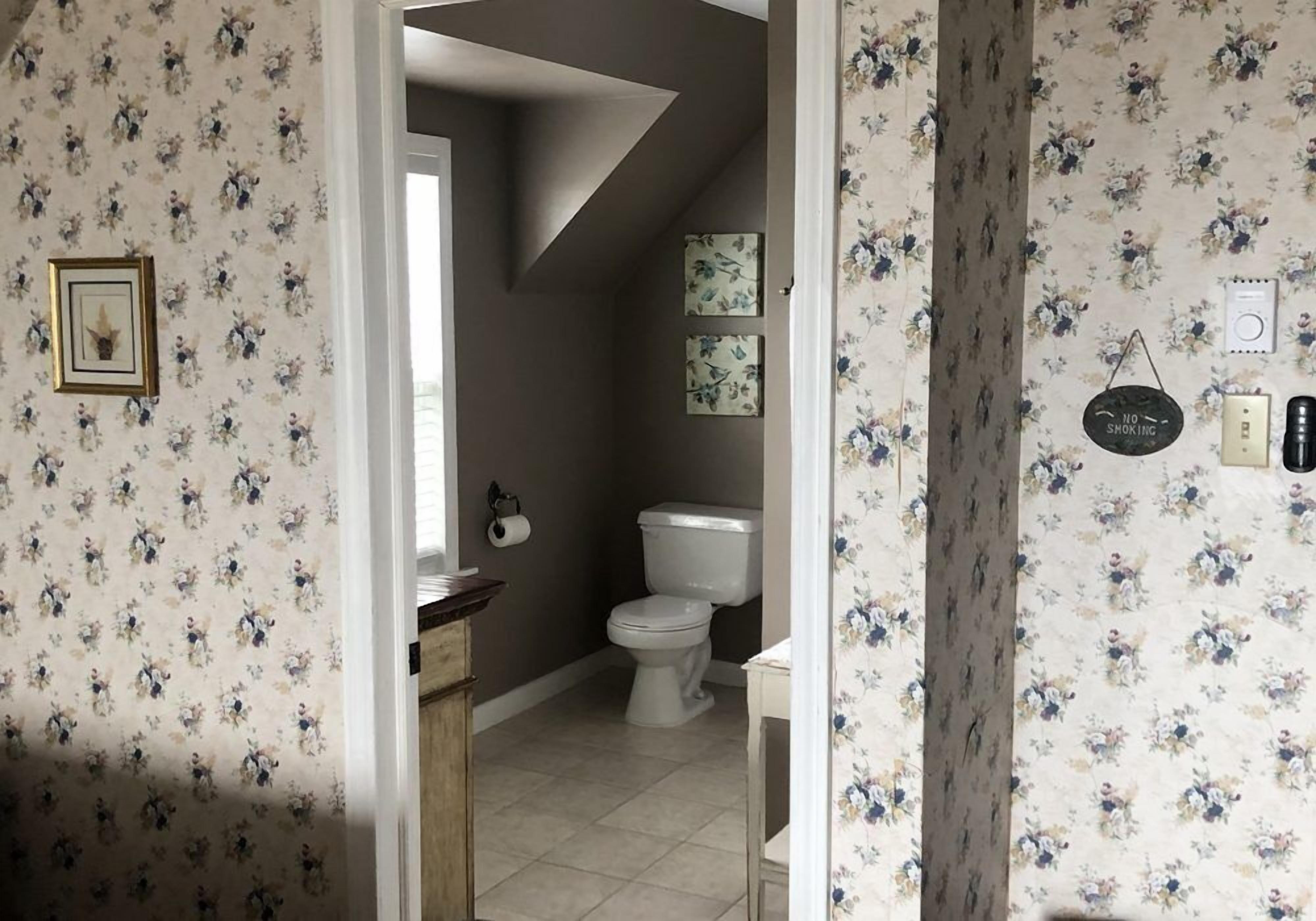 A bathroom with floral wallpaper, a toilet, a sink, and a shower.