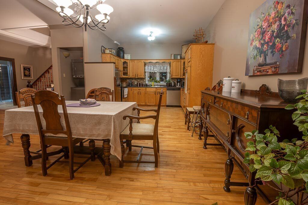 A dining area with a wooden table and chairs, a chandelier, and a kitchen in the background.