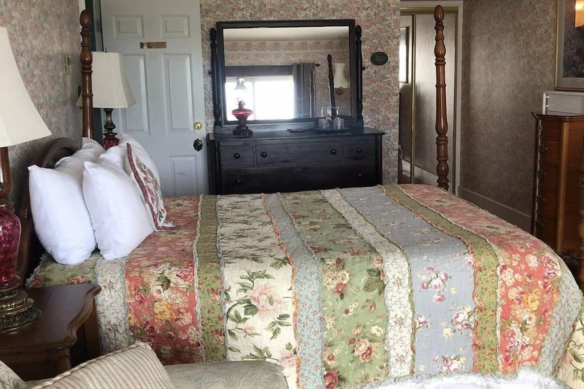 Un dormitorio con colcha estampada, cómoda con espejo y mesita de noche con lámpara.
