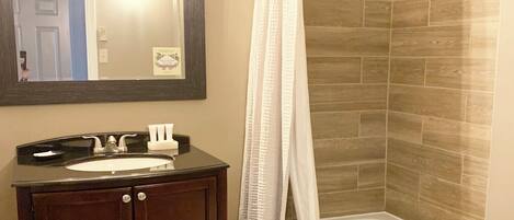 A bathroom with a dark wooden vanity, a white sink, and a mirror above it. There is a shower curtain and a bathtub with wooden wall tiles.