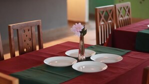 A dining table set with plates, a vase with a flower, and a green table runner. - Mercure Resorts Wayanad (Mananthavady)