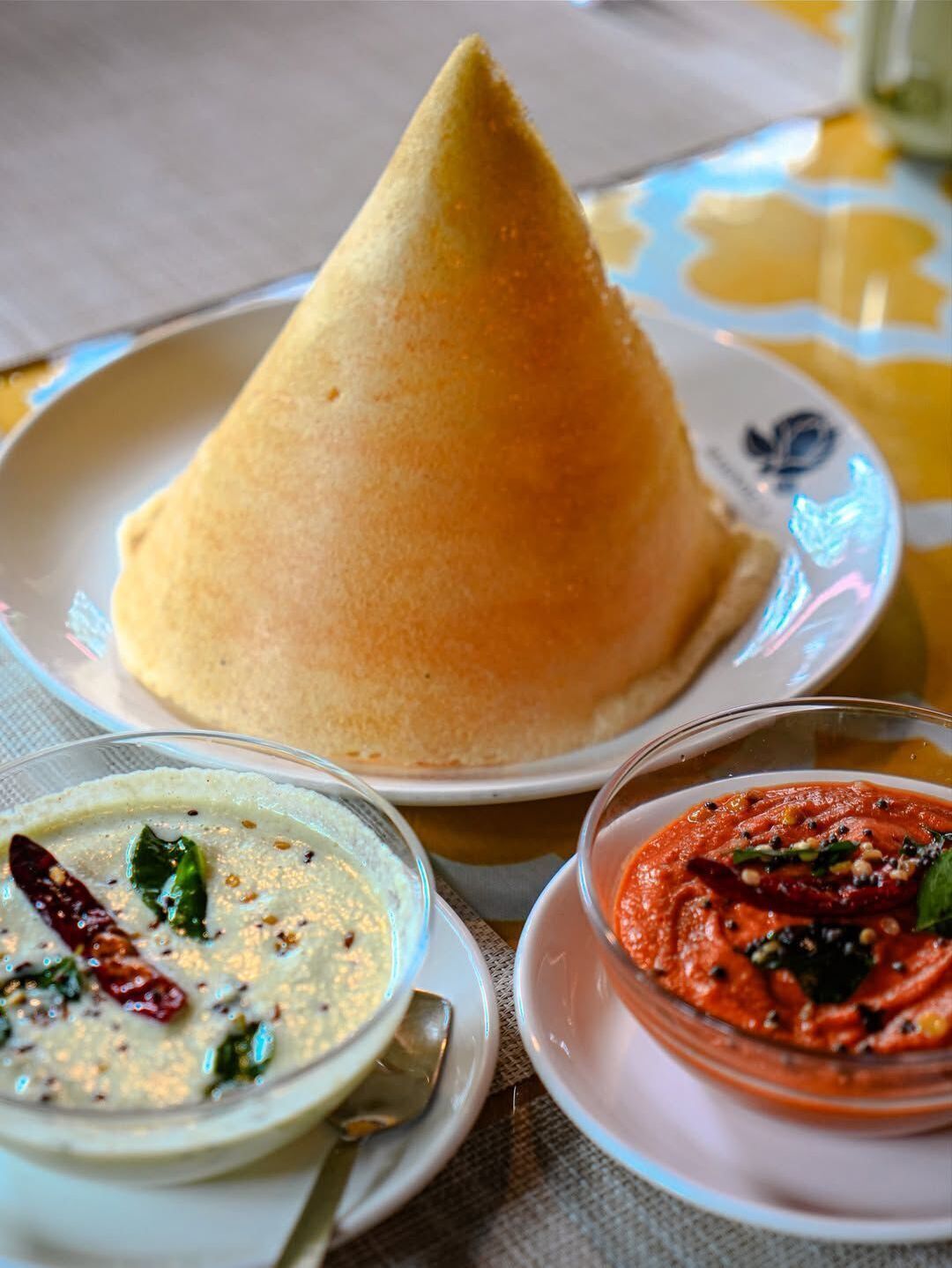 A meal with a cone-shaped food item, a bowl of white soup with herbs, and a bowl of red sauce.