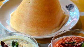A meal with a cone-shaped food item, a bowl of white soup with herbs, and a bowl of red sauce.
