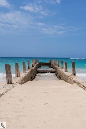 A concrete pier leading to a beach with clear turquoise water.
