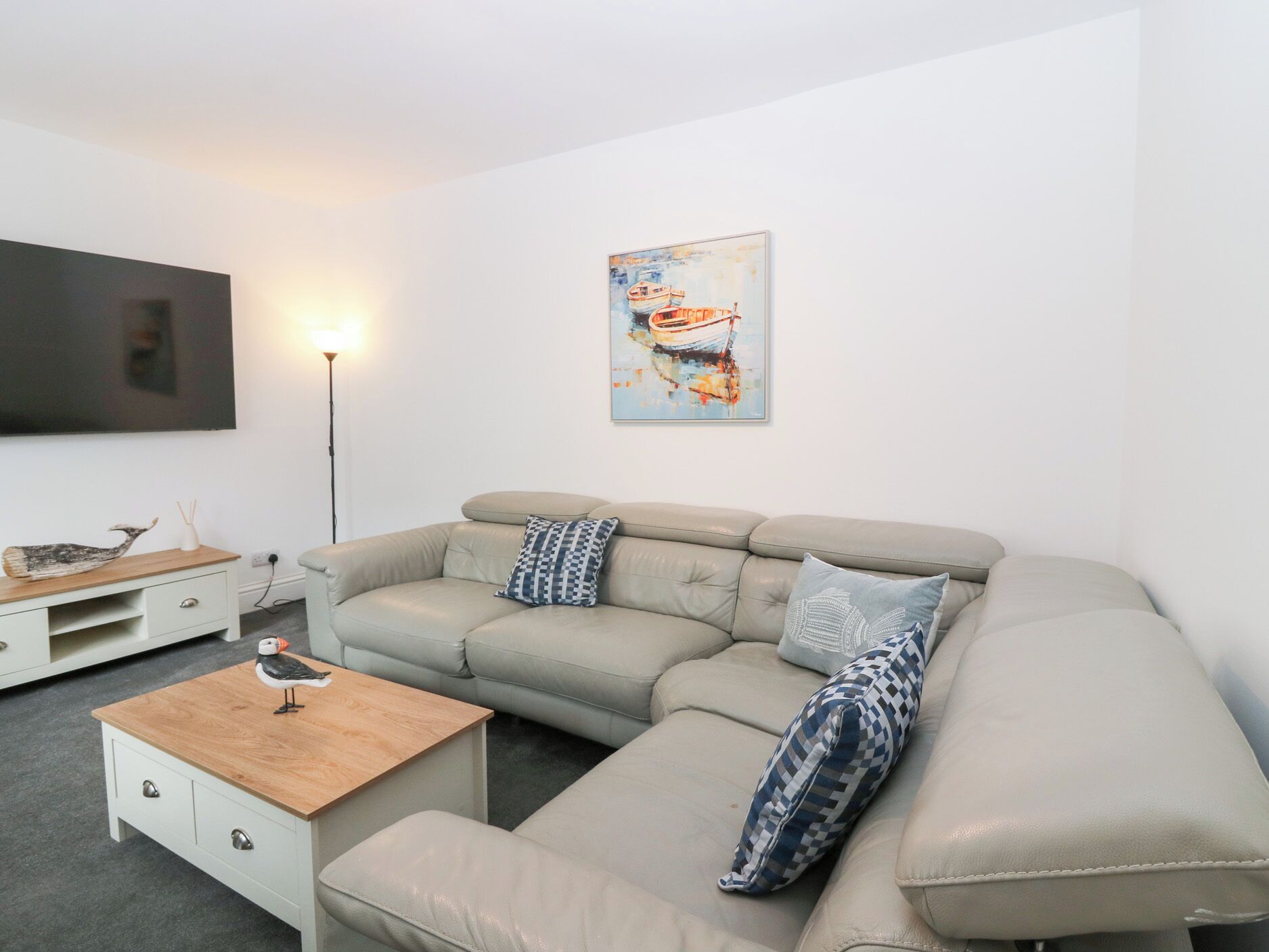 Un salon moderne avec un canapé d’angle beige, une table basse en bois et un téléviseur à écran plat fixé au mur.